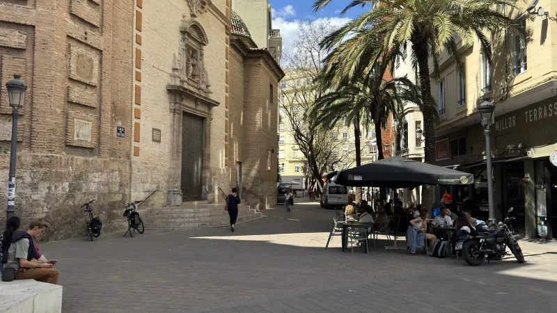 Terraza de un bar bajo palmeras, junto a una iglesia de fachada barroca