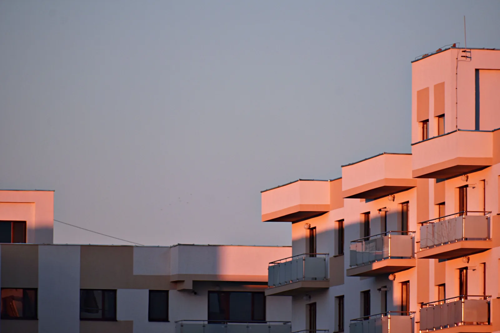 Fachada de un bloque de viviendas moderno con terrazas, iluminada por la luz del atardecer