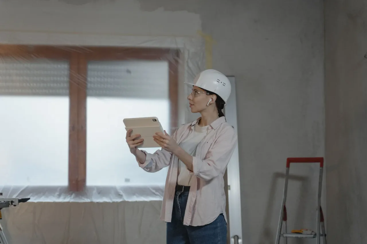 Técnica con casco y gafas de protección revisando un plano en una tablet dentro de una vivienda en reforma
